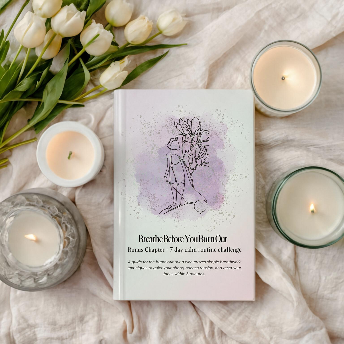 A book titled 'Breathe Before You Burn Out: Bonus Chapter: 7 day calm routine challenge' lies on a soft beige fabric, surrounded by lit candles and white tulips. The book cover has a white background with a light purple watercolor splash and a drawing of a woman meditating